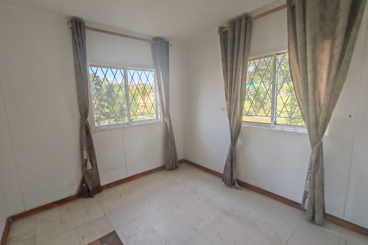 An empty bedroom featuring tiled flooring, security bars on the windows, and neutral walls, offering a blank canvas for potential renovation.