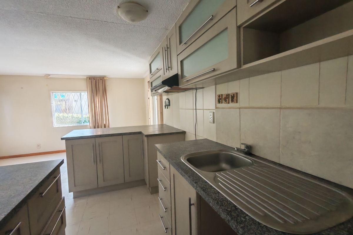 A functional kitchen featuring laminate cabinetry, stone-look countertops, a stainless steel sink, and tiled backsplash, offering a clean and neutral space for updates.