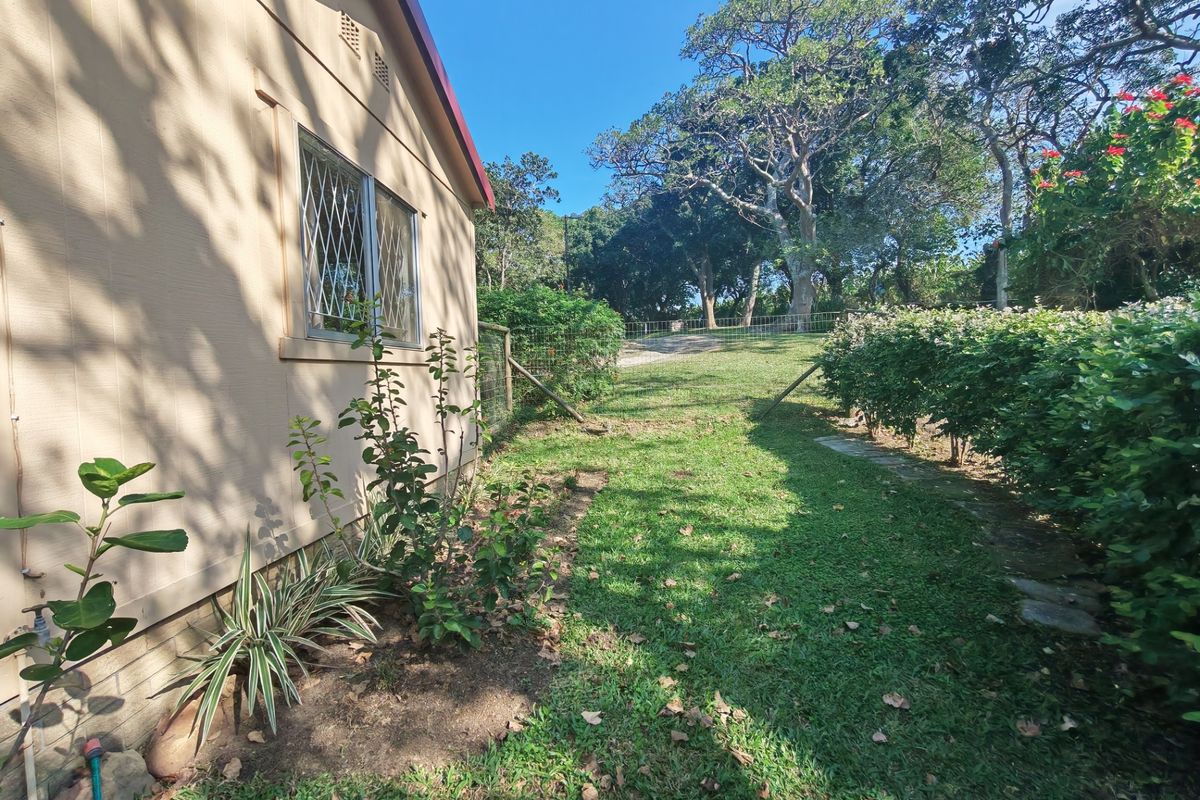 A view of the rear exterior of the property featuring a lawn, established garden beds, and security-fitted windows.