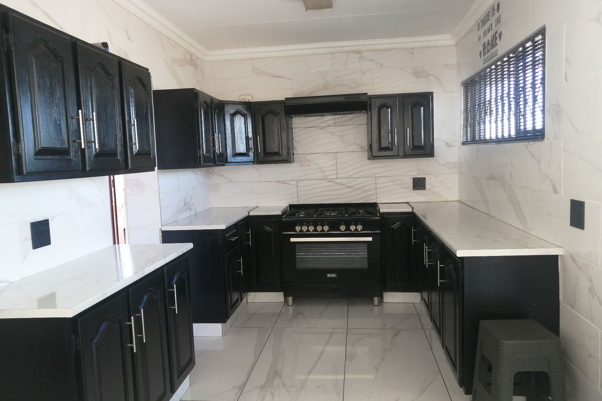Modern kitchen featuring black cabinetry, marble-look wall and floor tiles, and a built-in gas stove with an extractor fan.