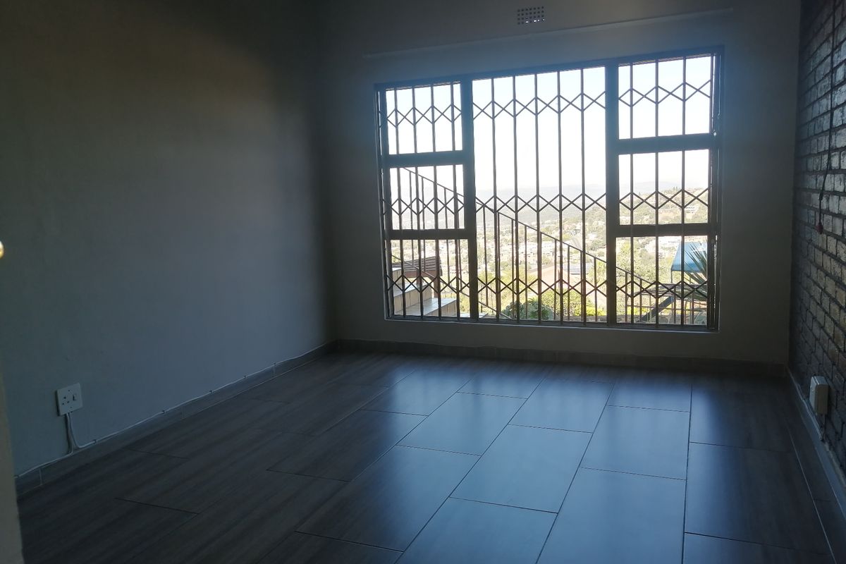 An empty bedroom featuring modern dark wood-look floor tiles, an exposed brick feature wall, and a large window with a security gate.