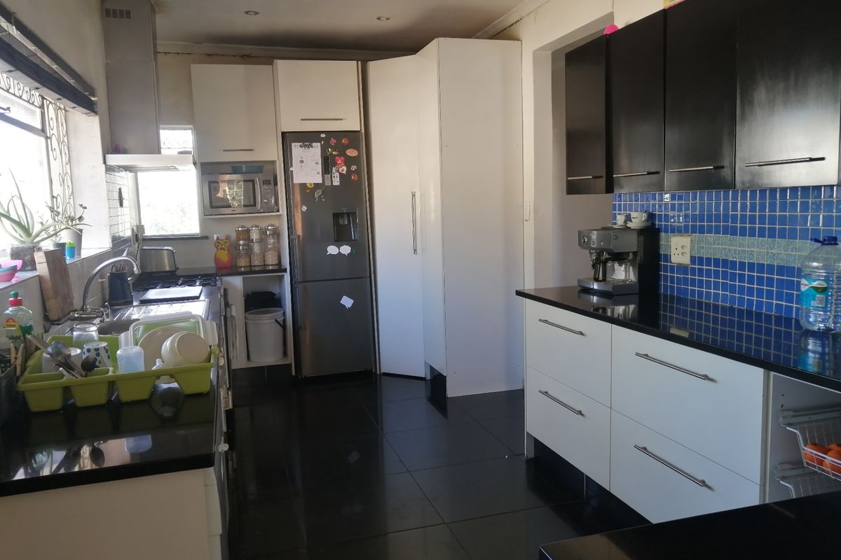 A functional kitchen featuring contrasting black and white cabinetry, granite countertops, a blue tiled backsplash, and dark floor tiles.
