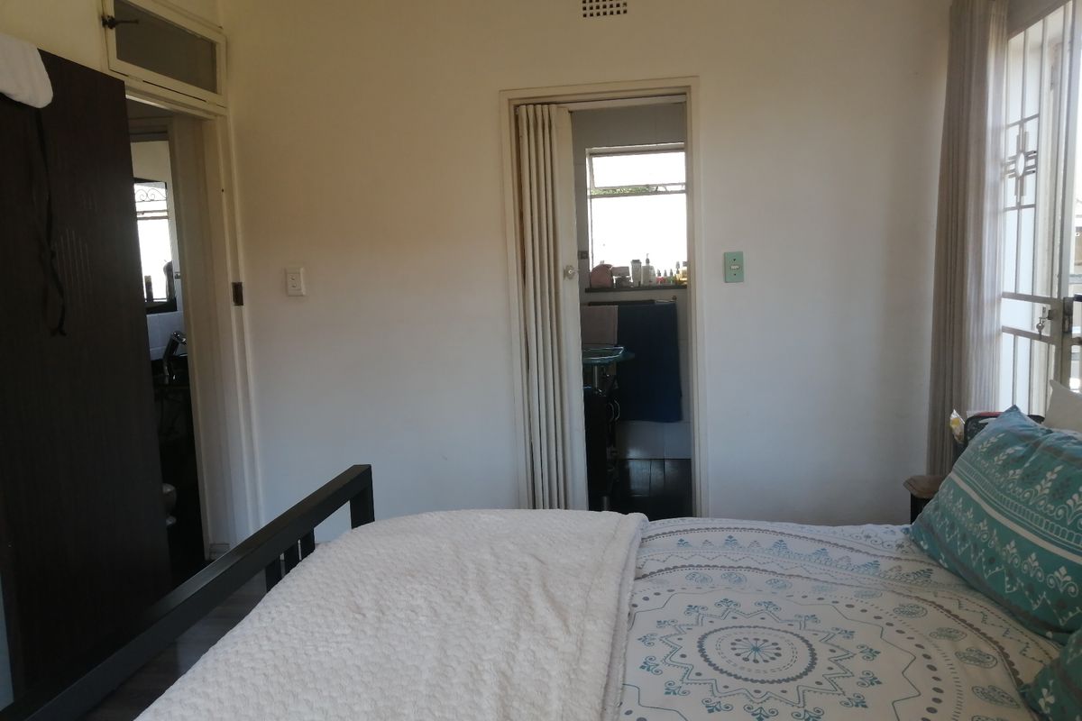 A bedroom featuring a folding door leading to an en-suite bathroom, a built-in wardrobe, and a security gate on the window.