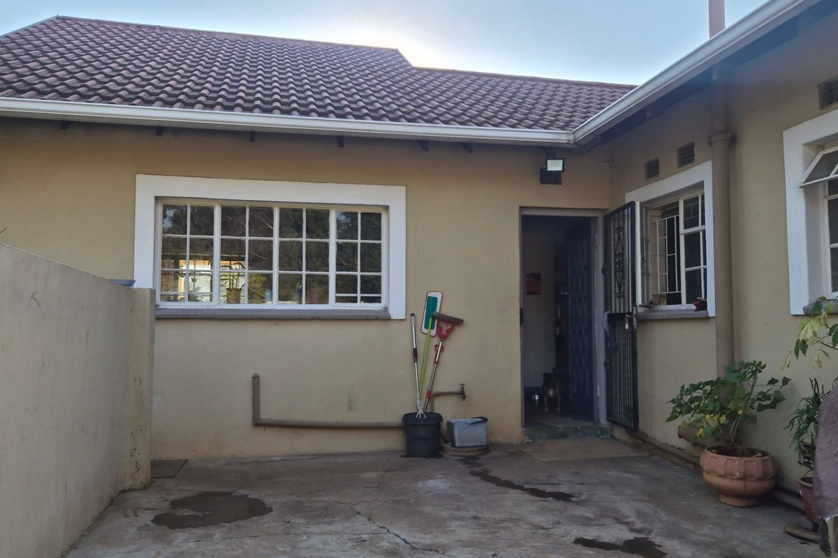 Rear exterior view of the property featuring a concrete patio area, tiled roof, and security access door.