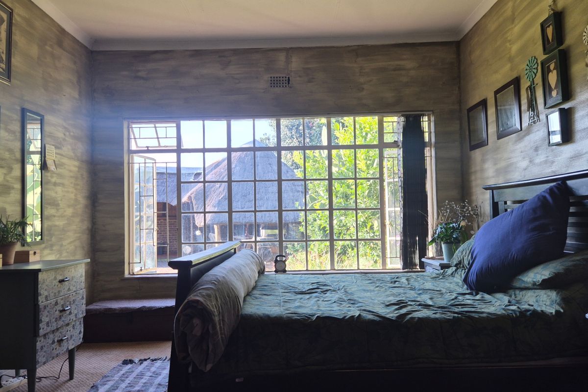 A bedroom featuring a large steel-framed window with garden views and unique textured wall finishes.