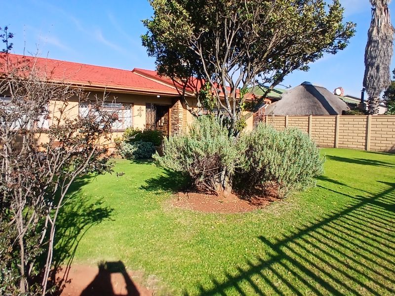 A view of the rear garden featuring a well-maintained lawn, mature trees, and a brick boundary wall, adjacent to the house exterior.