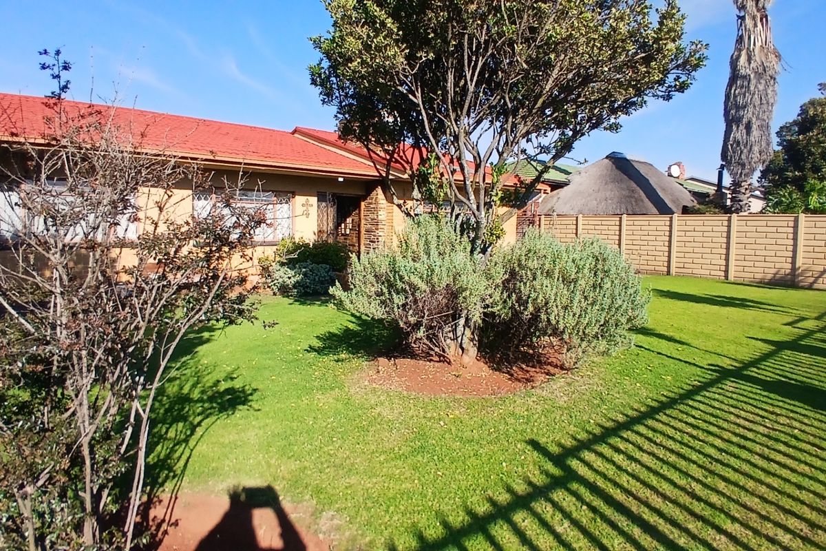 A view of the rear garden featuring a well-maintained lawn, mature trees, and a brick boundary wall, adjacent to the house exterior.
