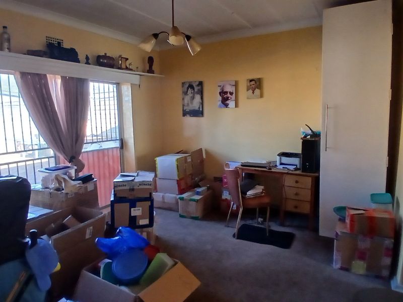 A bedroom featuring built-in cabinetry, carpeted flooring, and a sliding door with security bars, currently used as a storage and workspace area.