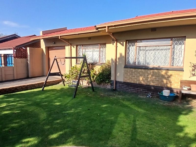 Front exterior view of a single-story house featuring a lawn, brick and plaster facade, and security bars on windows.