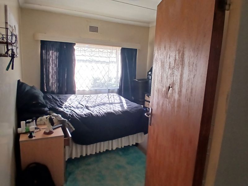 A compact bedroom featuring a window with security bars and a wooden door showing signs of wear.