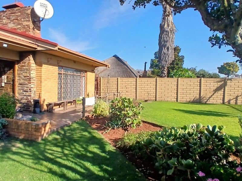 A view of the rear garden featuring a paved patio area, established lawn, and perimeter boundary wall.
