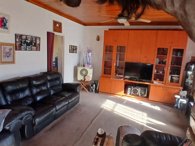 A living room featuring a built-in wooden wall unit, timber ceiling with a fan, and carpeted flooring.