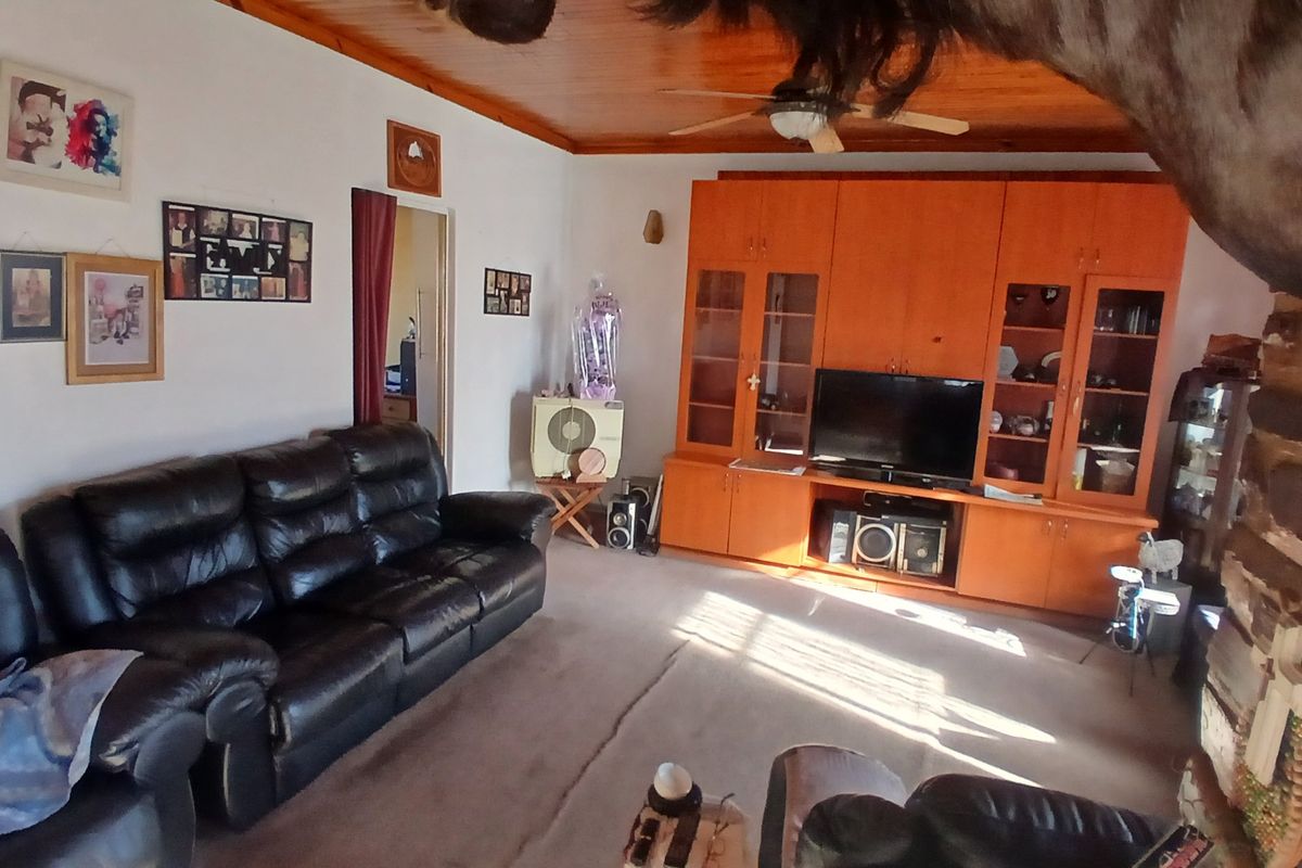 A living room featuring a built-in wooden wall unit, timber ceiling with a fan, and carpeted flooring.