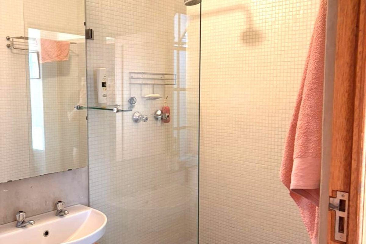 A compact bathroom featuring a glass-enclosed shower with mosaic tiling, a modern vessel sink on a wooden vanity, and dark stone flooring.