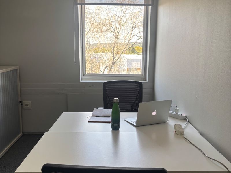 A functional office space featuring carpet flooring, a window with a roller blind, and integrated electrical infrastructure.