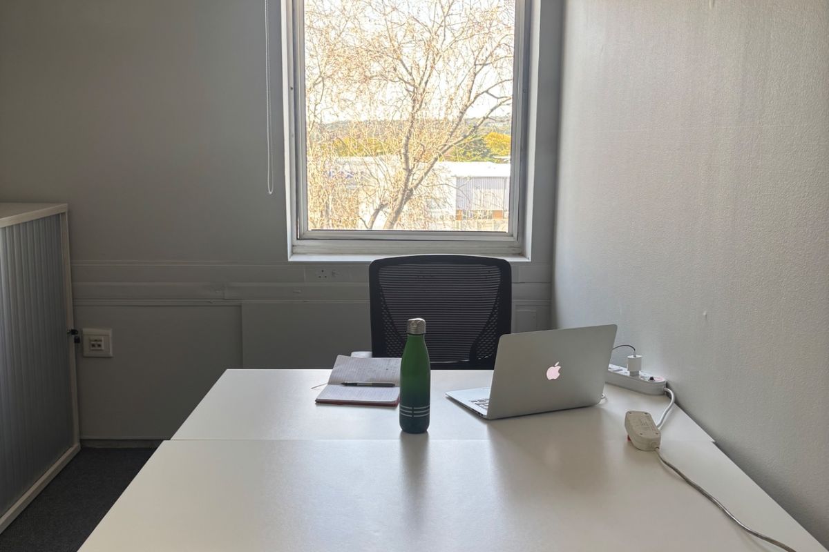 A functional office space featuring carpet flooring, a window with a roller blind, and integrated electrical infrastructure.