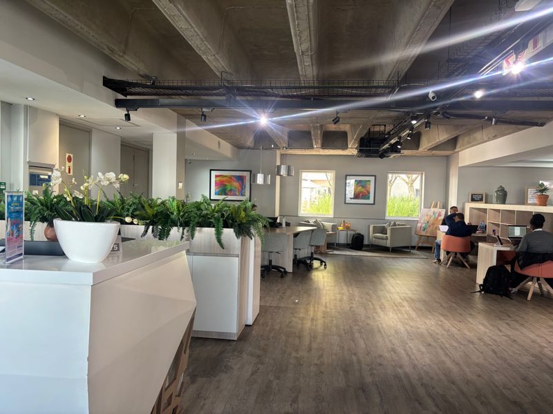 Modern open-plan commercial office space featuring exposed concrete ceilings, track lighting, and durable laminate flooring with integrated reception and storage areas.