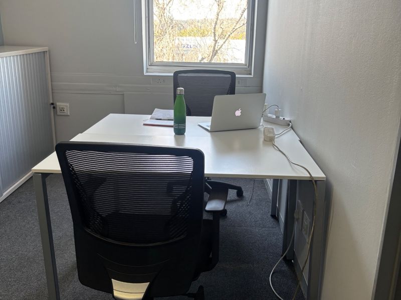 A functional office space featuring carpeted flooring, a window with a roller blind, and built-in storage cabinetry.