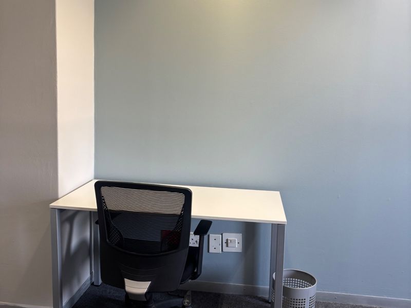 A compact office space featuring neutral blue accent wall, recessed ceiling lighting, and integrated electrical and data connectivity points.