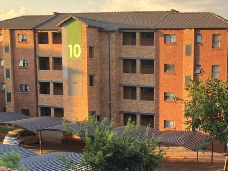 A multi-story apartment building featuring a face brick exterior, tiled roofing, and dedicated carport parking bays for residents.