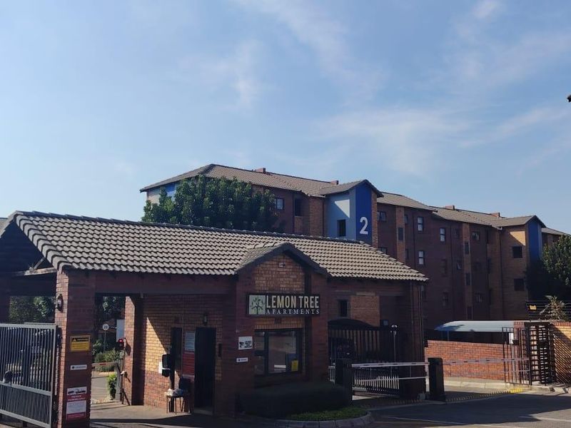 The entrance to Lemon Tree Apartments featuring a brick guard house, security gate, and boom access control for the residential complex.