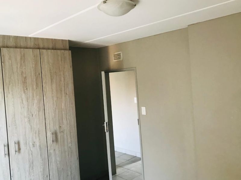 A clean, empty bedroom featuring a modern wood-finish built-in wardrobe and neutral wall tones, providing a versatile space ready for personalization.