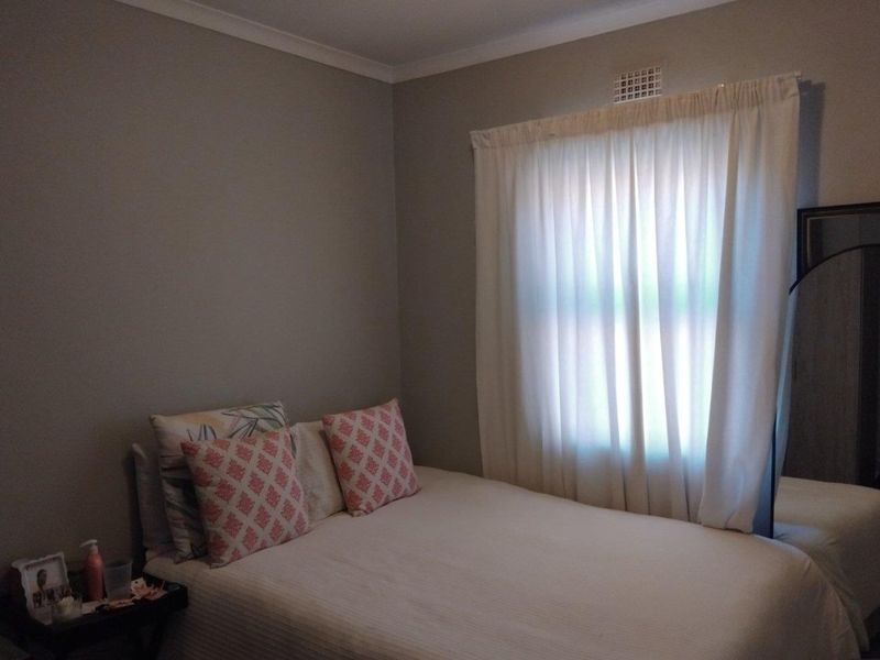 A standard bedroom featuring neutral wall paint, a window with curtain treatments, and a built-in ventilation grille.