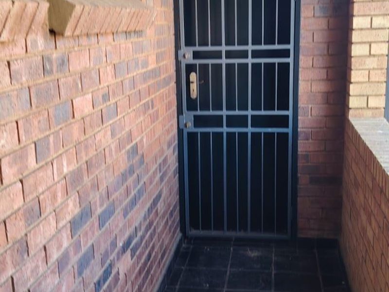 A secure apartment entrance featuring a black metal security gate, exposed brick walls, and dark tiled flooring.