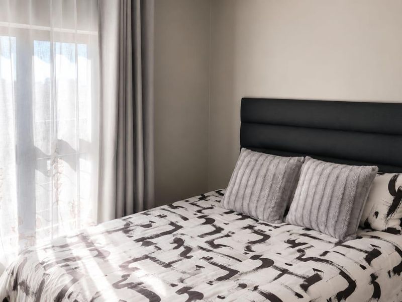 A well-lit bedroom featuring neutral wall tones and large windows with installed curtain tracks, providing a bright and comfortable living space.
