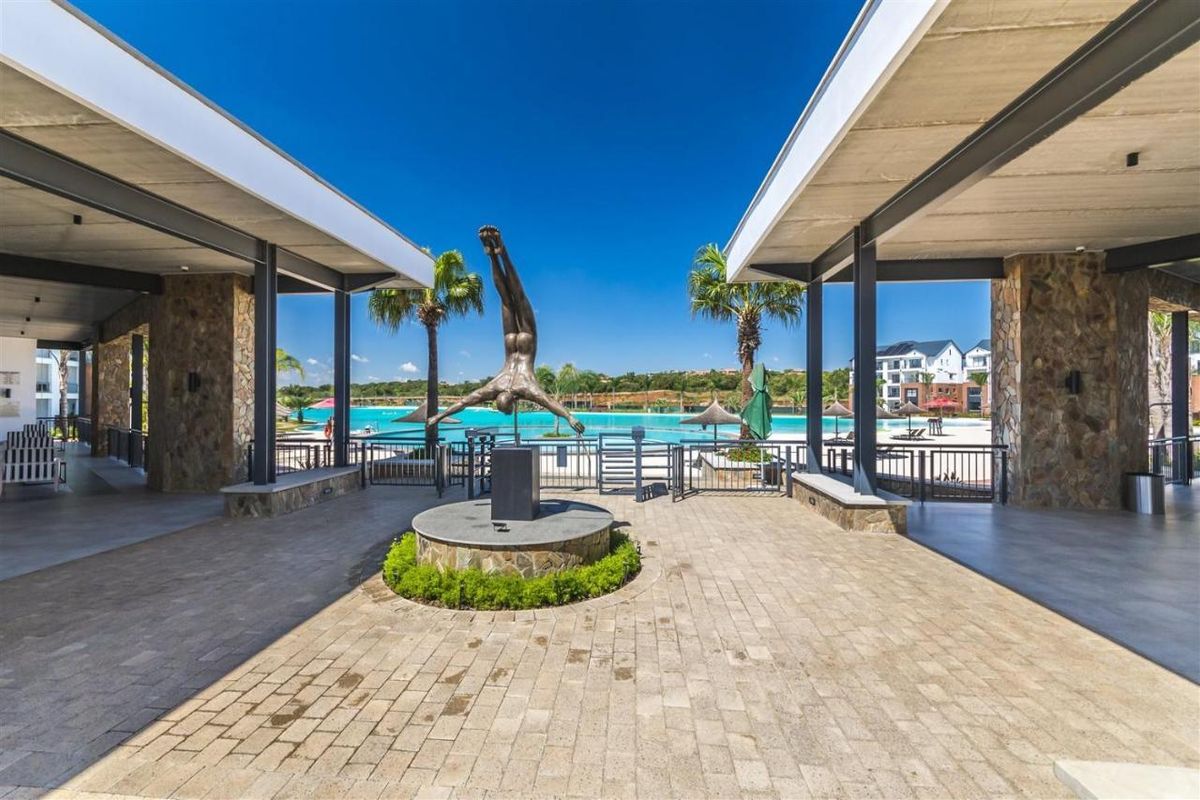 A well-maintained outdoor pool area featuring a central sculpture, paved courtyard, and covered walkways with stone-clad pillars overlooking the swimming pool.