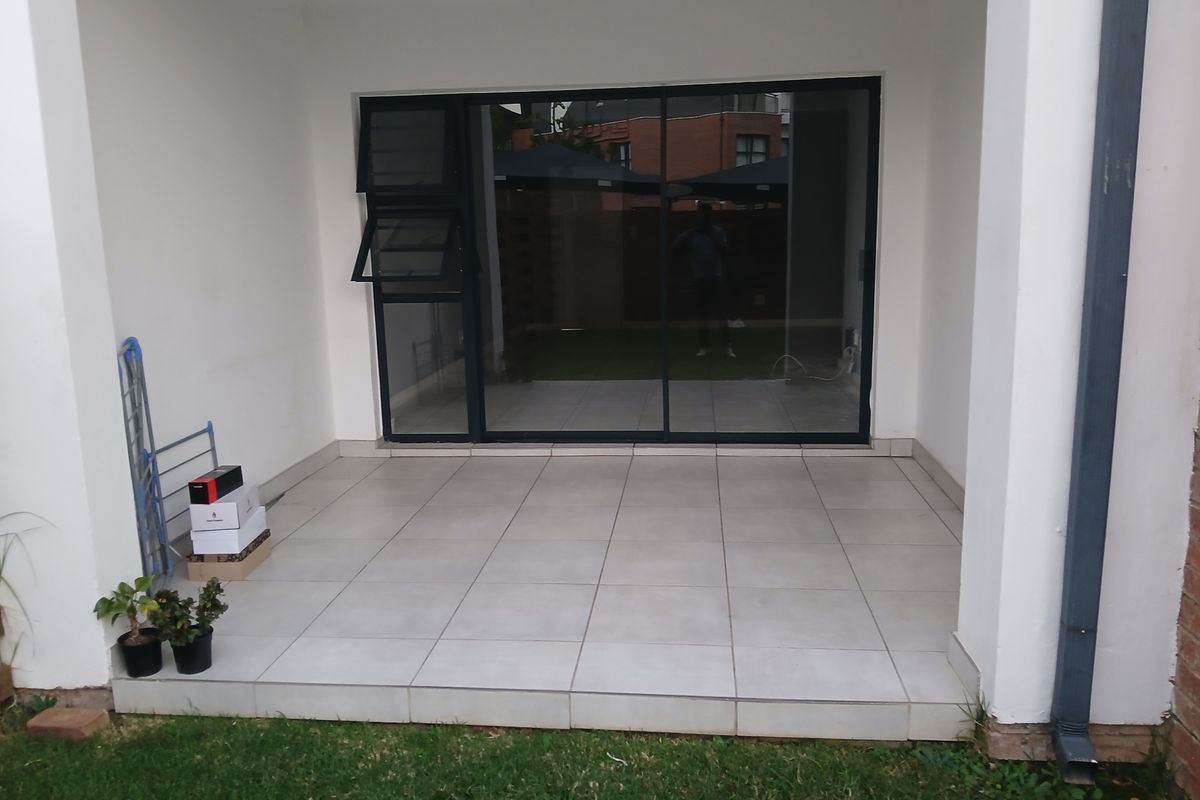 A covered patio area featuring neutral floor tiles and a large sliding glass door providing access to the interior living space.