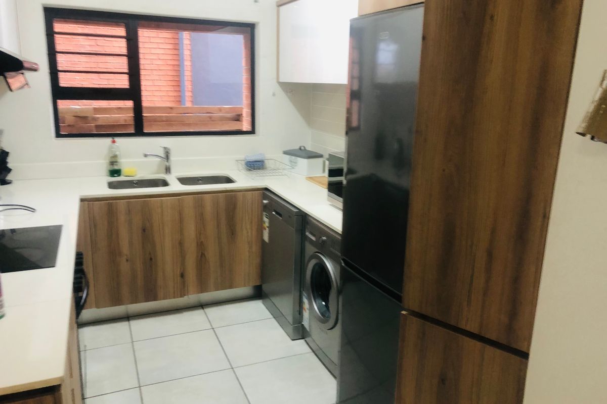 Modern kitchen featuring wood-look cabinetry, white stone countertops, double sink, and tiled flooring with a functional layout.