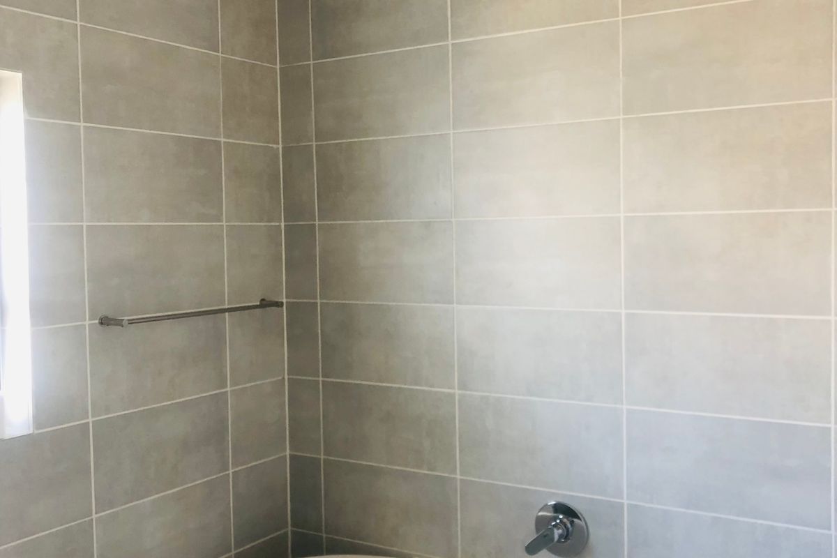 A clean, modern bathroom featuring neutral wall tiles, a built-in bathtub, and chrome fixtures.