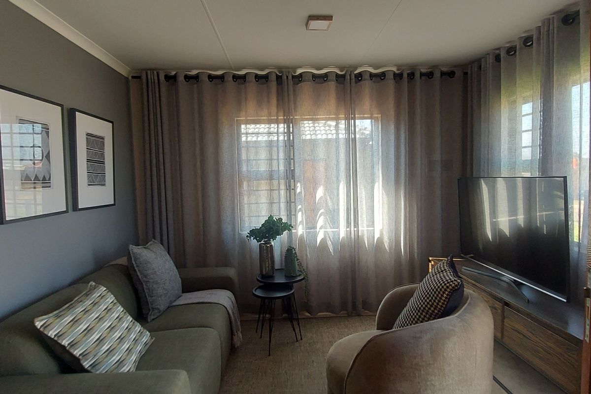 A cozy living room featuring neutral grey walls, large windows with floor-to-ceiling curtains, and a comfortable seating arrangement.