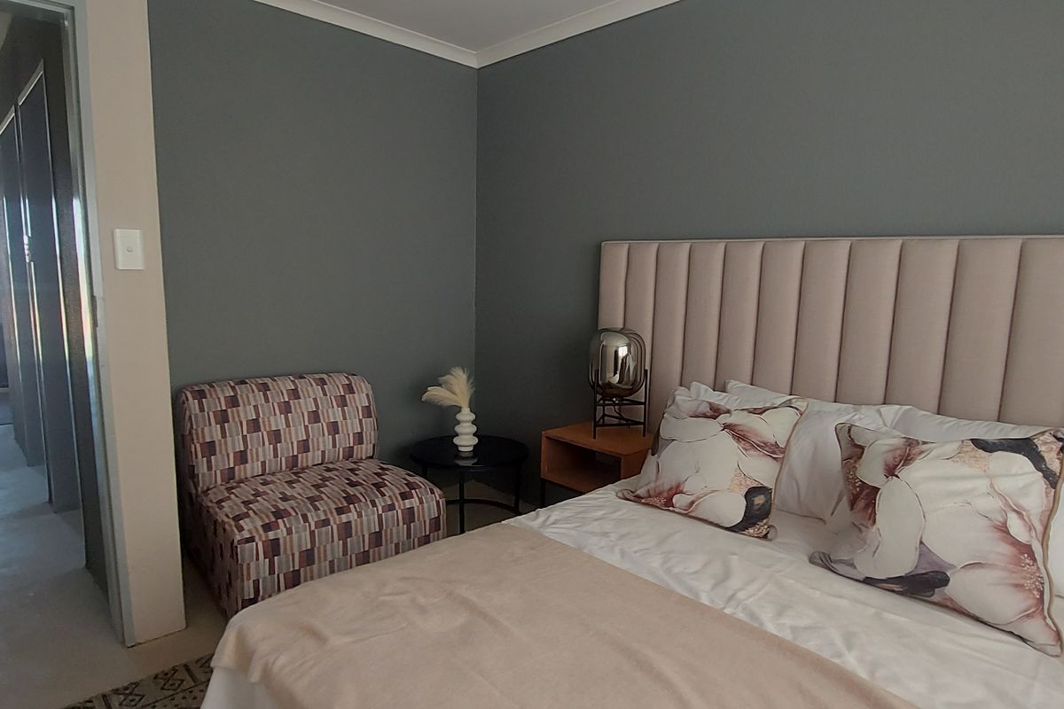 A well-maintained bedroom featuring a large upholstered headboard and neutral grey wall tones, with an adjacent hallway visible.