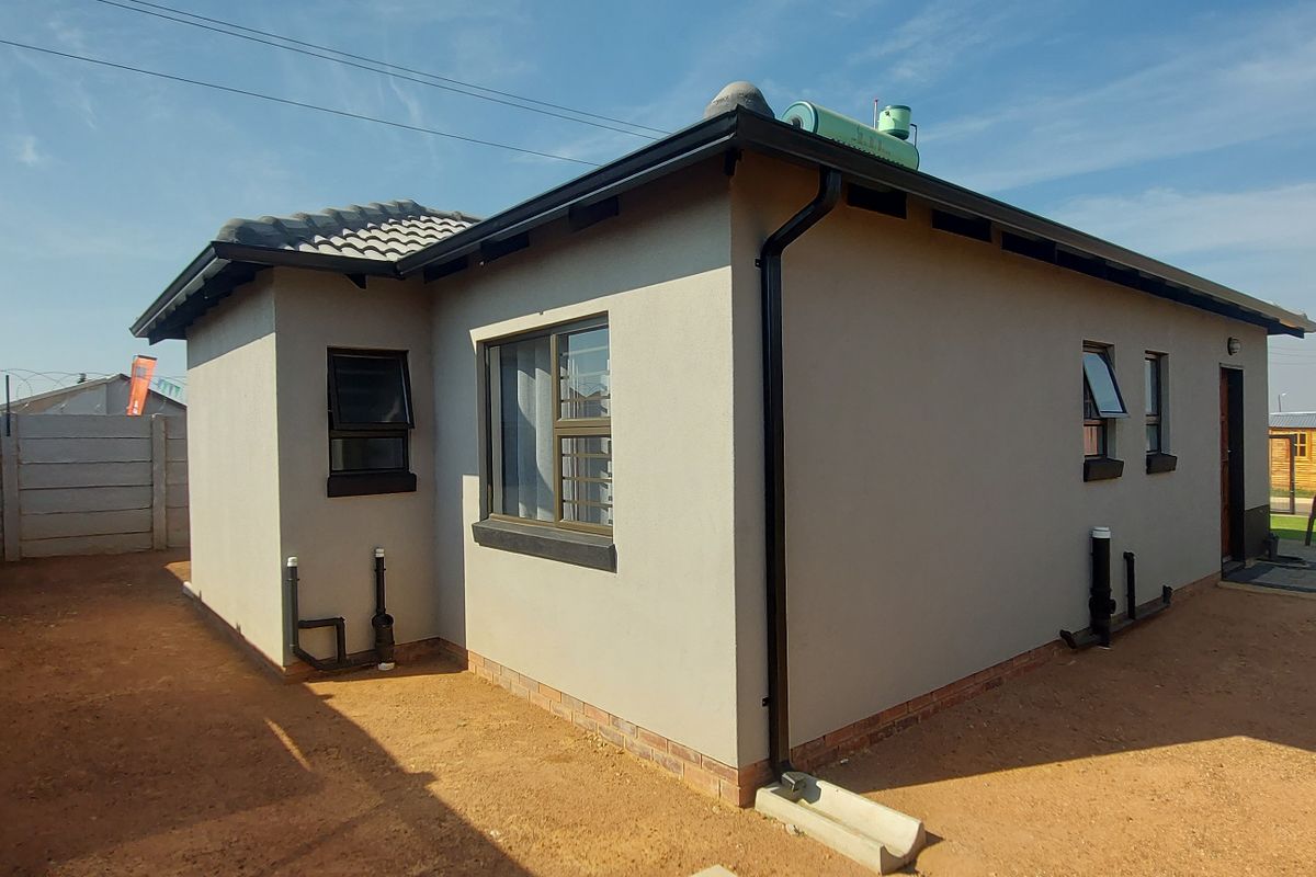 Rear view of a modern single-story house featuring a solar geyser, concrete roof tiles, and a precast concrete boundary wall.