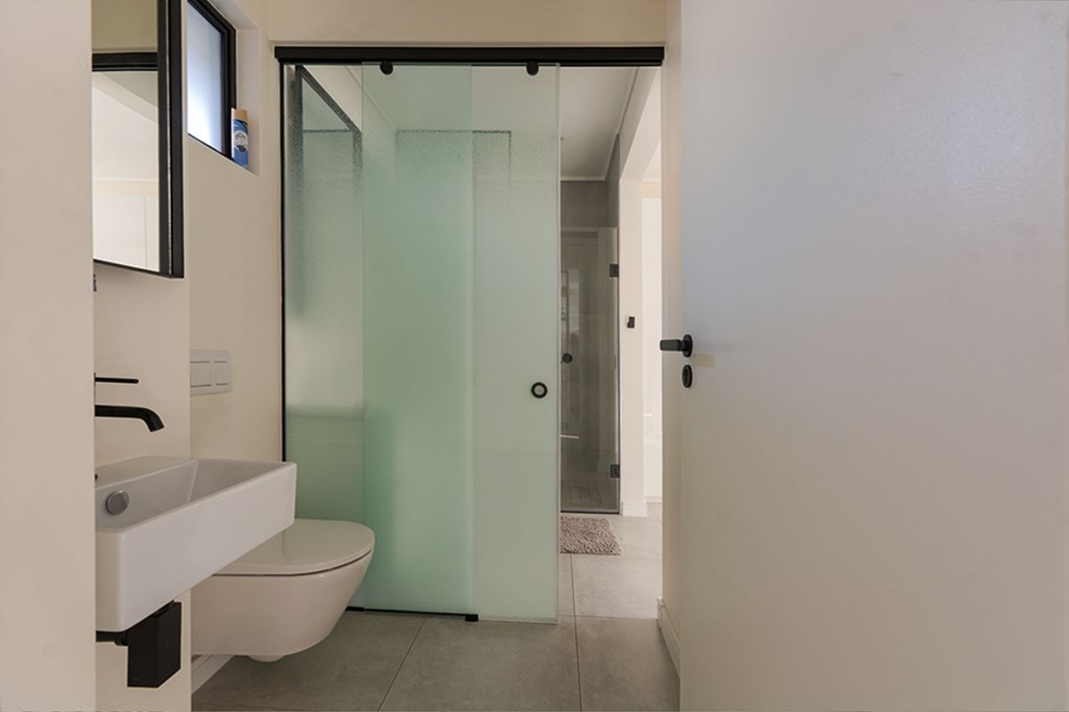 Modern bathroom featuring a wall-mounted basin, wall-hung toilet, and a sleek sliding frosted glass door leading to a walk-in shower area.