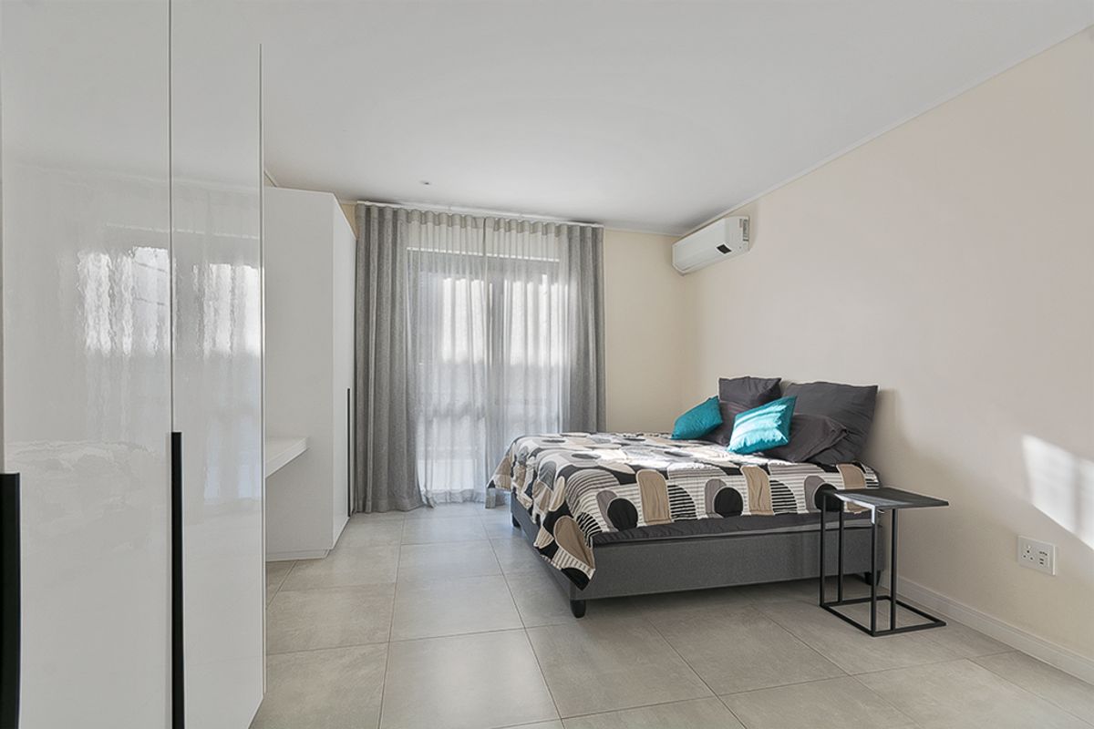 A bright and modern bedroom featuring large format floor tiles, built-in white cabinetry, and a split-system air conditioner with access to a private balcony.