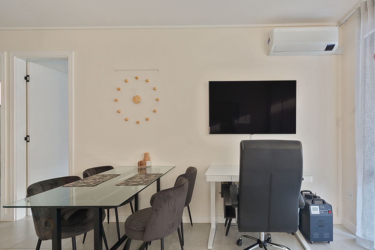 A well-maintained living area featuring tiled flooring, a wall-mounted air conditioning unit, and a wall-mounted television.