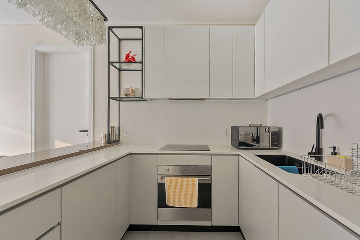Modern U-shaped kitchen featuring sleek white cabinetry, integrated appliances, a black undermount sink, and a convenient breakfast bar for casual dining.
