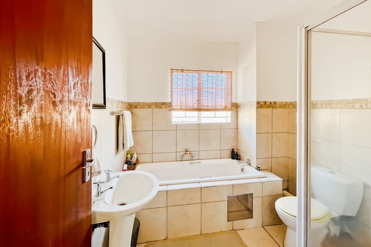 A functional bathroom featuring a pedestal basin, built-in bathtub, separate shower enclosure, and toilet with neutral wall and floor tiling.