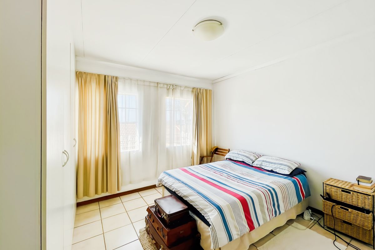 A functional bedroom featuring built-in cupboards, tiled flooring, and natural light through large windows.