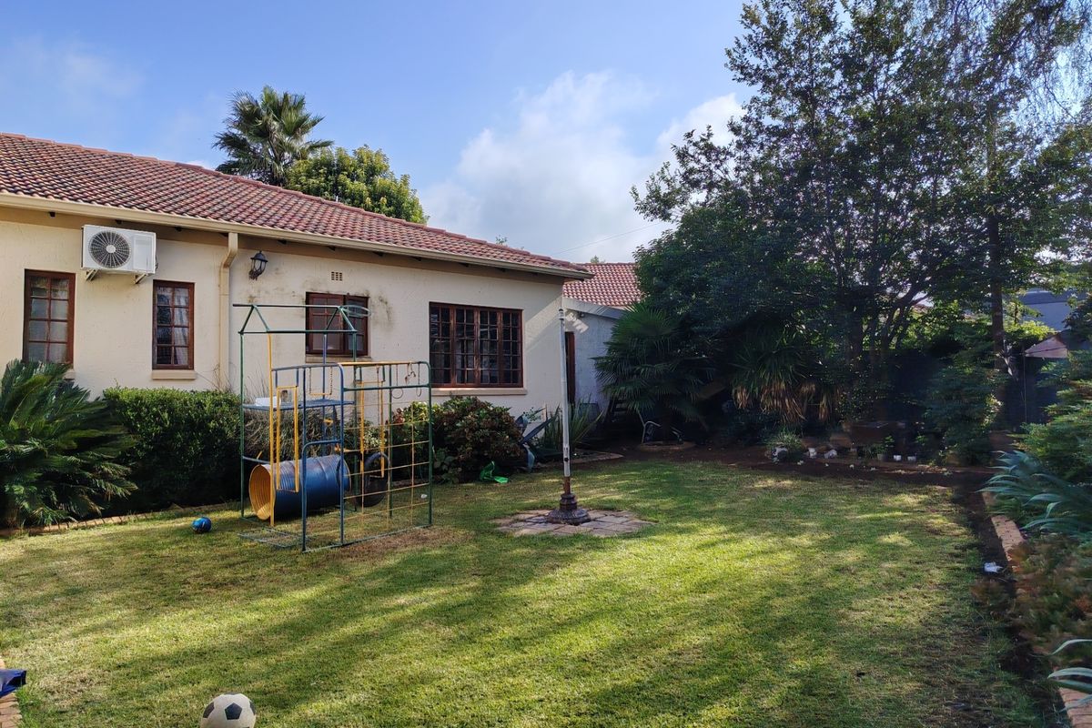 Rear view of the property featuring a spacious lawn, mature garden landscaping, and a tiled roof structure with an exterior air conditioning unit.
