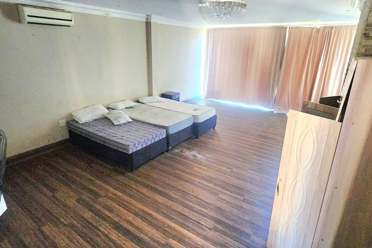 Spacious bedroom featuring laminate flooring, a split-system air conditioner, and a decorative stone-cladding pillar, requiring cosmetic updates to improve its overall appeal.