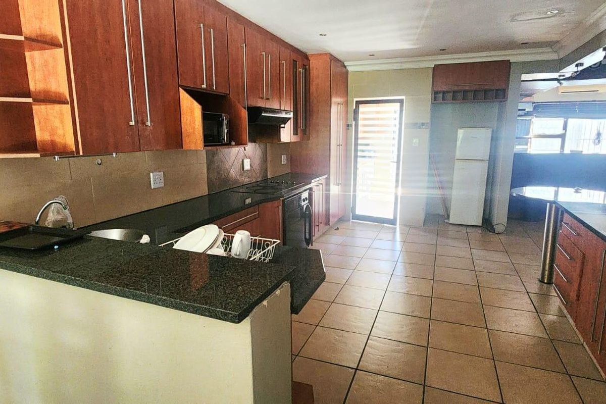 A functional kitchen featuring granite countertops, wooden cabinetry, and ceramic floor tiles, with direct access to the exterior.