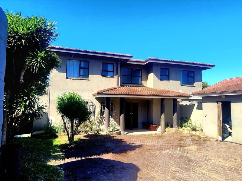 Rear view of a two-story house featuring a paved courtyard, covered entrance with columns, and an adjacent garage with a water tank.
