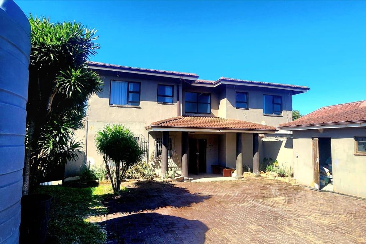 Rear view of a two-story house featuring a paved courtyard, covered entrance with columns, and an adjacent garage with a water tank.