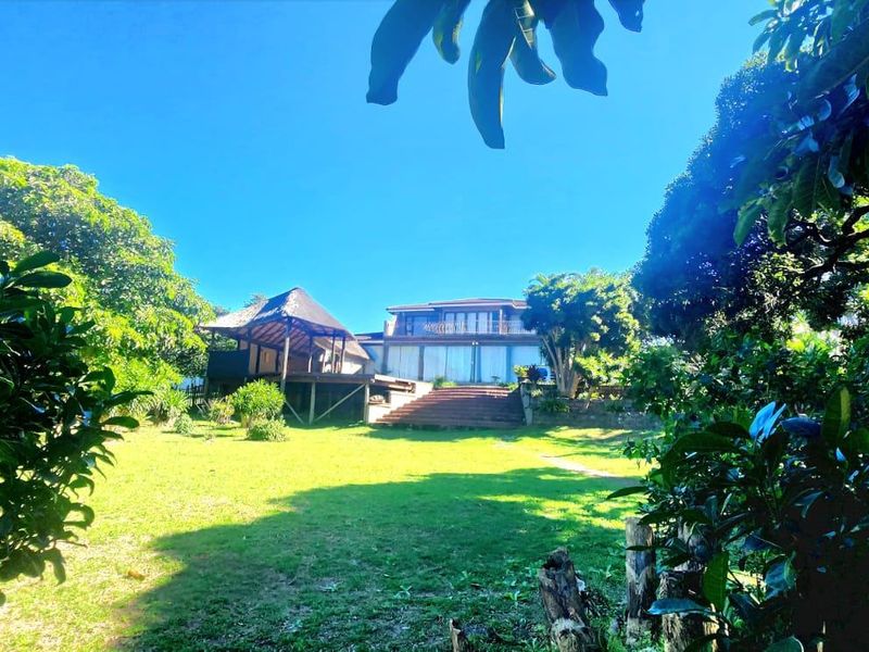 A view of the rear elevation featuring a spacious lawn, a thatched gazebo, and timber decking leading to the main residence.