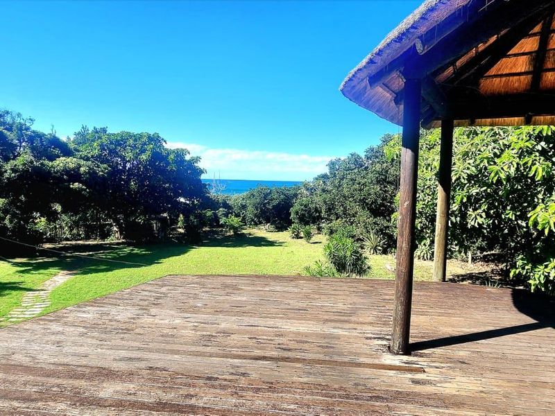 Covered outdoor timber deck with a thatched roof, overlooking a spacious garden with distant ocean views.