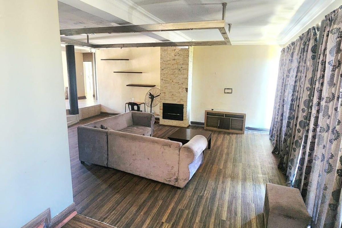 Spacious living room featuring a stone-clad fireplace, laminate flooring, and a unique ceiling bulkhead, offering a versatile layout for comfortable family living.